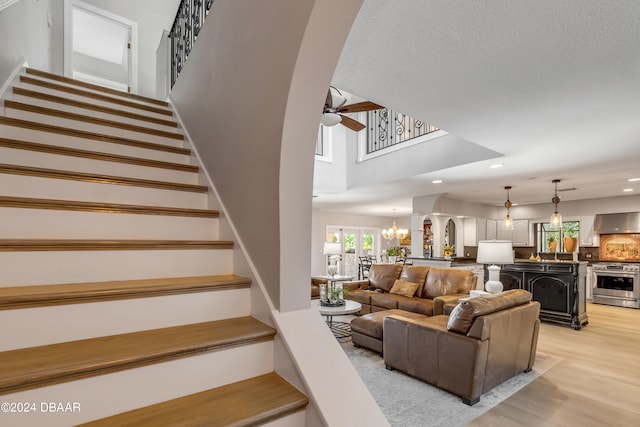 living room featuring a textured ceiling, light wood-type flooring, a towering ceiling, and ceiling fan with notable chandelier