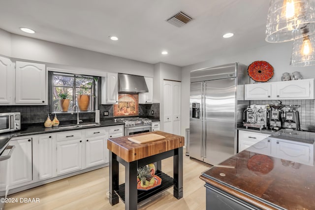 kitchen featuring light hardwood / wood-style floors, high end appliances, white cabinets, wall chimney exhaust hood, and sink