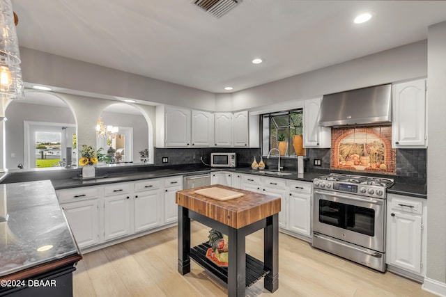 kitchen with light hardwood / wood-style flooring, wall chimney range hood, appliances with stainless steel finishes, and white cabinets