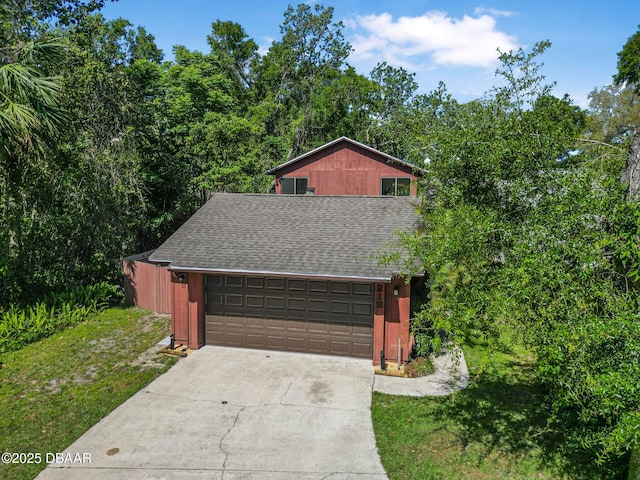 view of front of house with roof with shingles, concrete driveway, a front yard, and an attached garage