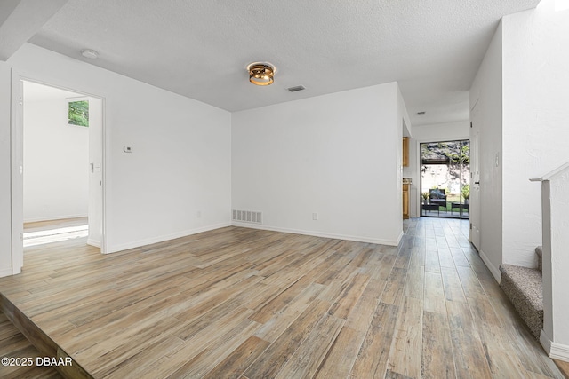 unfurnished room featuring visible vents, light wood-type flooring, and a textured ceiling
