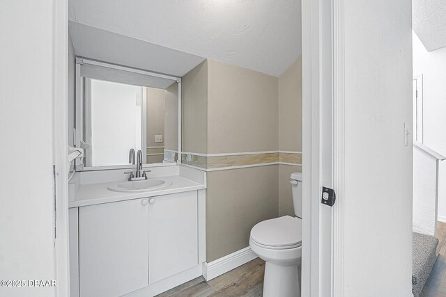 bathroom featuring a textured ceiling, baseboards, toilet, wood finished floors, and vanity