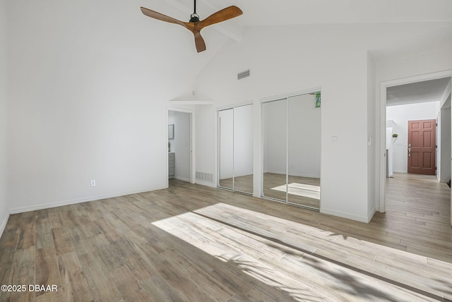 unfurnished bedroom featuring visible vents, wood finished floors, multiple closets, and high vaulted ceiling