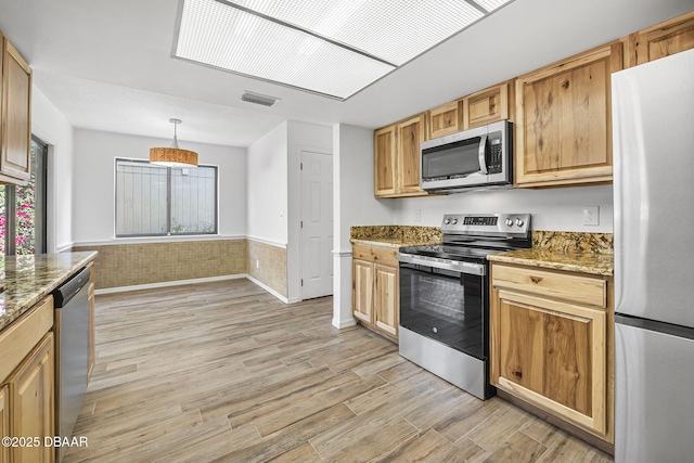 kitchen with light stone counters, light wood-style floors, appliances with stainless steel finishes, a wainscoted wall, and visible vents