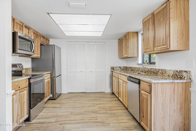 kitchen featuring light stone countertops, stainless steel appliances, light wood finished floors, a sink, and visible vents