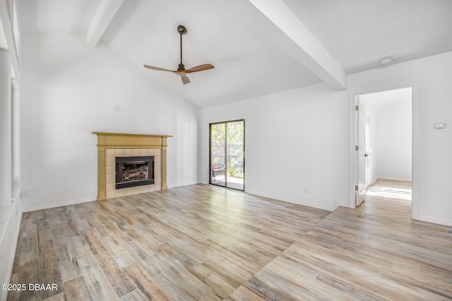 unfurnished living room featuring a tiled fireplace, lofted ceiling with beams, a ceiling fan, baseboards, and wood finished floors