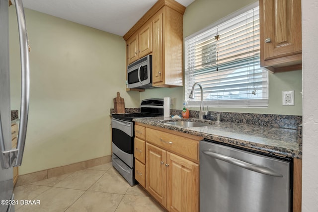 kitchen featuring stainless steel appliances, dark stone counters, sink, and light tile patterned floors