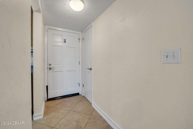 hall with a textured ceiling and light tile patterned floors