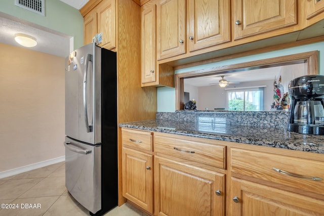 kitchen with dark stone counters, ceiling fan, stainless steel refrigerator, and light tile patterned floors