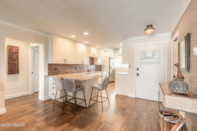 kitchen with a kitchen bar, ornamental molding, wood finished floors, and stainless steel fridge with ice dispenser