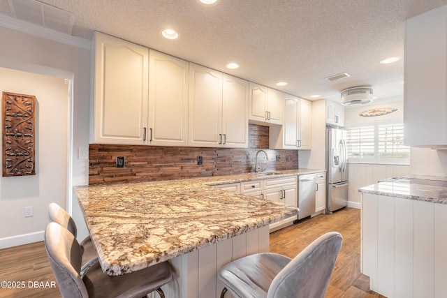 kitchen with dishwashing machine, a breakfast bar, a peninsula, stainless steel refrigerator with ice dispenser, and a sink