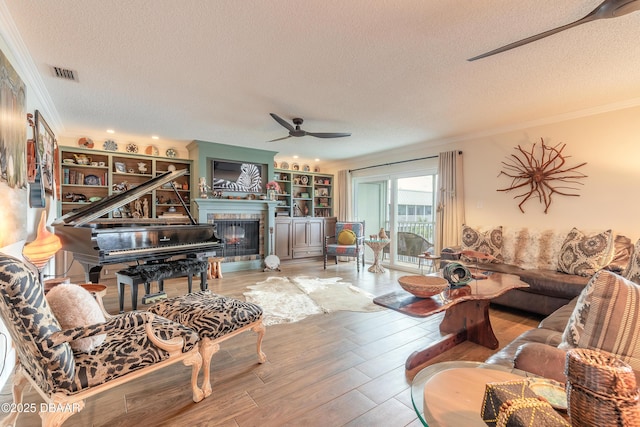 living area featuring visible vents, wood finished floors, a textured ceiling, crown molding, and a fireplace