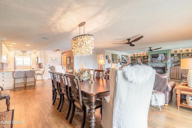 dining space featuring visible vents, an inviting chandelier, a textured ceiling, light wood-type flooring, and a fireplace