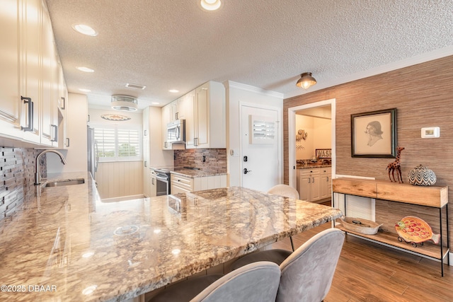 kitchen with light stone counters, a sink, visible vents, appliances with stainless steel finishes, and a kitchen bar