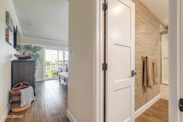 hallway featuring a textured ceiling, wood finished floors, visible vents, baseboards, and crown molding