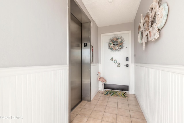 doorway with elevator, wainscoting, a textured ceiling, and light tile patterned flooring