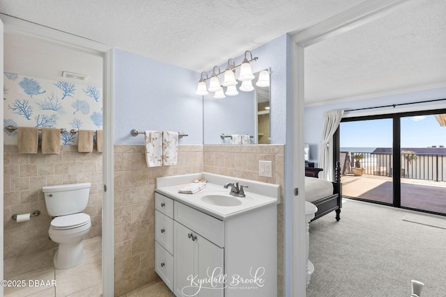 bathroom featuring tile walls, vanity, toilet, and a textured ceiling