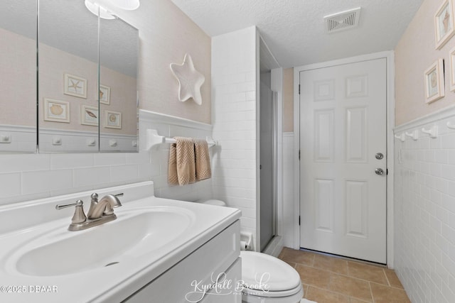 bathroom featuring a textured ceiling, tile walls, vanity, a shower with door, and tile patterned flooring