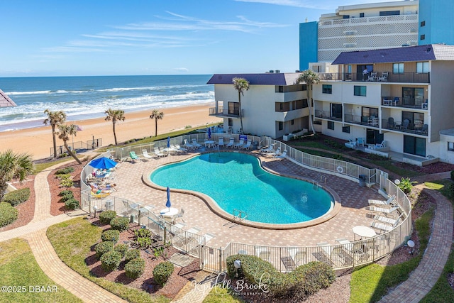 view of swimming pool featuring a water view, a beach view, and a patio area