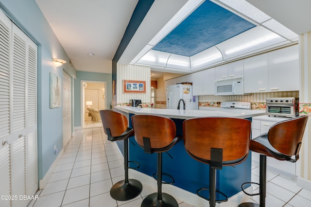 kitchen featuring a kitchen breakfast bar, white cabinetry, light tile patterned floors, and white appliances