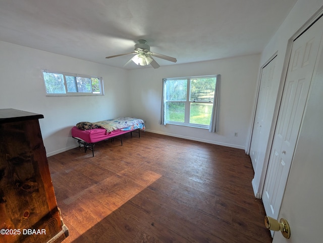 bedroom with baseboards, two closets, ceiling fan, and dark wood-style flooring