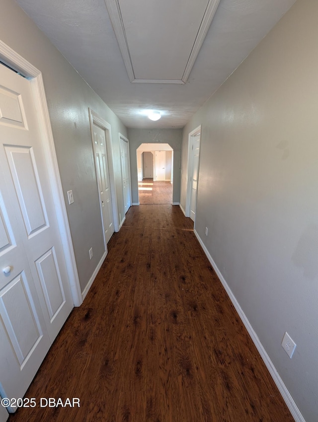corridor featuring attic access, baseboards, dark wood-style flooring, and arched walkways