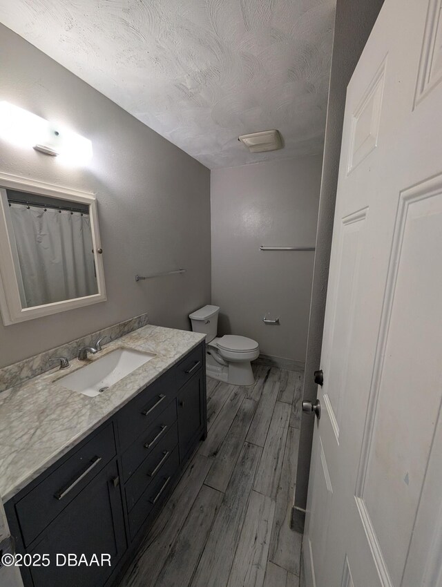 bathroom featuring a textured ceiling, toilet, vanity, and wood finished floors
