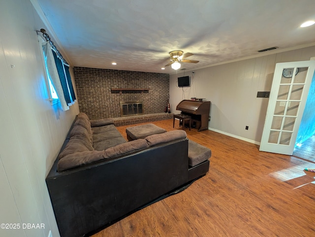 living room featuring visible vents, crown molding, a fireplace, wood finished floors, and a ceiling fan