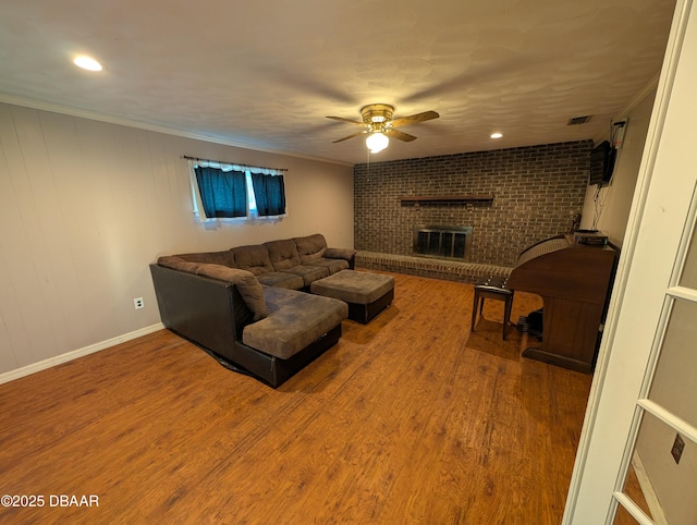 living area featuring visible vents, a brick fireplace, ceiling fan, ornamental molding, and wood finished floors