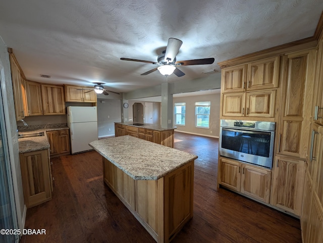 kitchen with a kitchen island, dark wood-type flooring, ceiling fan, stainless steel oven, and freestanding refrigerator