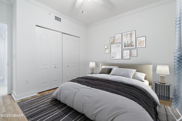 bedroom featuring wood finished floors, visible vents, baseboards, ornamental molding, and a closet