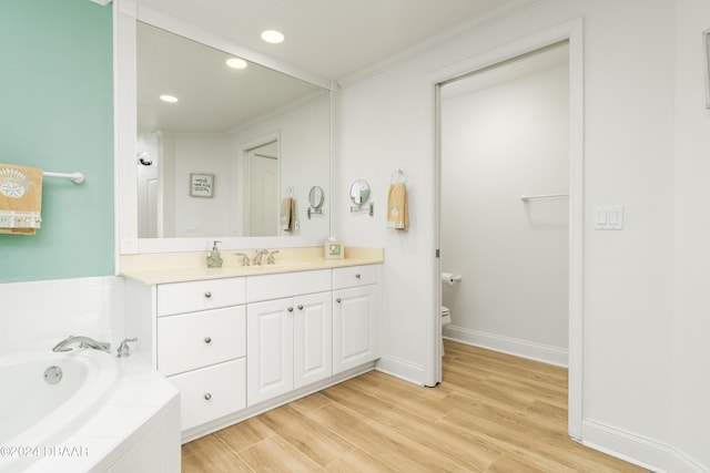 bathroom featuring tiled tub, crown molding, wood-type flooring, toilet, and vanity