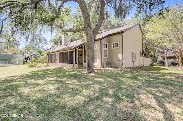 back of house with a sunroom, a chimney, stucco siding, central air condition unit, and a lawn