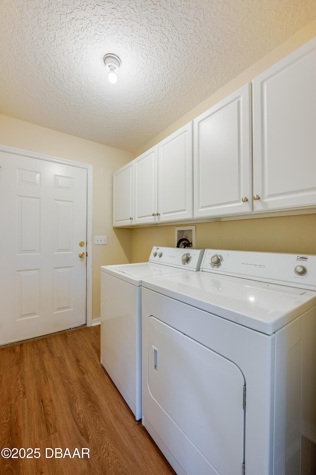 washroom with light wood-style floors, a textured ceiling, cabinet space, and washer and clothes dryer