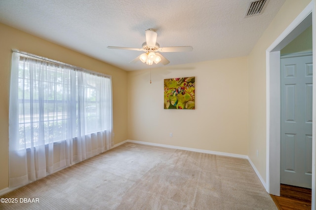 carpeted empty room featuring baseboards, a textured ceiling, ceiling fan, and visible vents