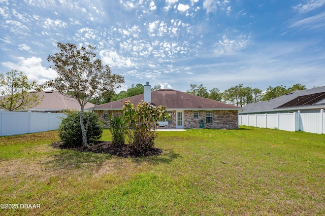 back of house featuring stone siding, a patio, a fenced backyard, a chimney, and a yard