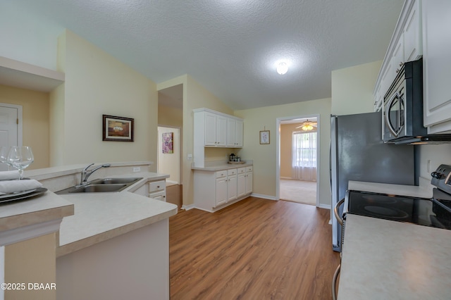 kitchen with appliances with stainless steel finishes, a sink, white cabinetry, light wood-type flooring, and vaulted ceiling