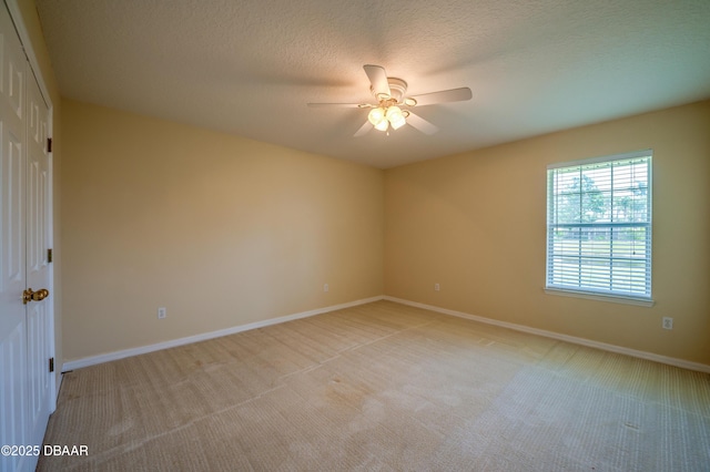 spare room featuring a ceiling fan, baseboards, light carpet, and a textured ceiling