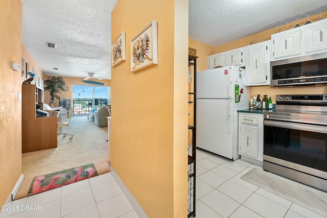 kitchen featuring light tile patterned floors, a textured ceiling, stainless steel appliances, and white cabinets