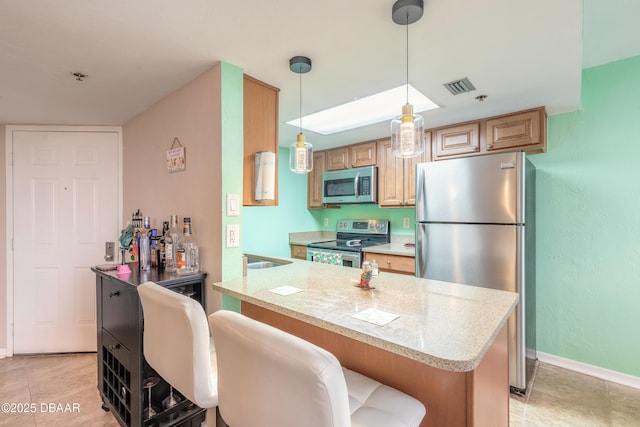 kitchen featuring appliances with stainless steel finishes, decorative light fixtures, kitchen peninsula, a breakfast bar, and light stone counters