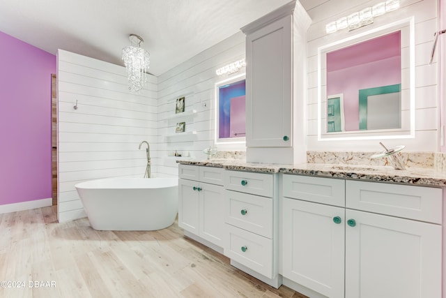 bathroom with wood walls, wood-type flooring, vanity, a chandelier, and a bathtub