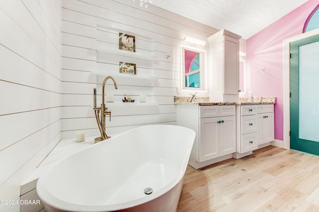 bathroom featuring a bath, hardwood / wood-style flooring, vanity, and wooden walls