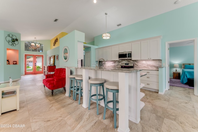 kitchen featuring tasteful backsplash, french doors, white cabinetry, appliances with stainless steel finishes, and decorative light fixtures