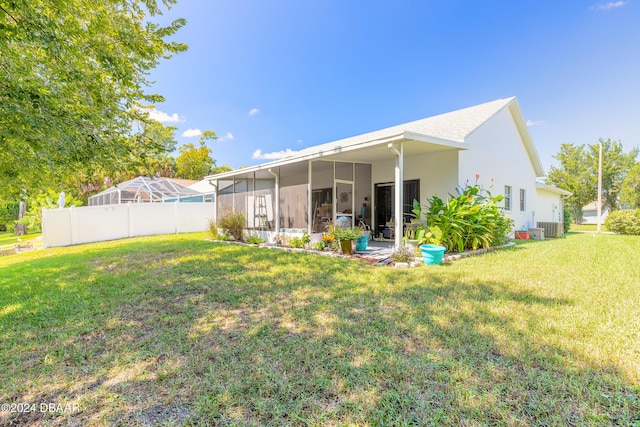 rear view of property featuring central AC unit, a lawn, a sunroom, and glass enclosure