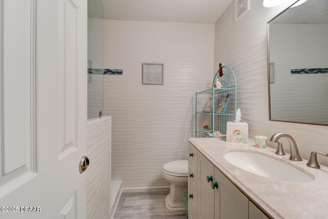 bathroom with vanity, a textured ceiling, a shower, hardwood / wood-style floors, and toilet