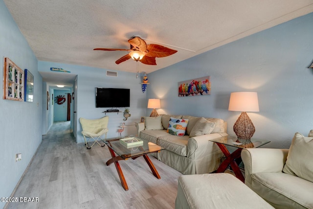 living room featuring ceiling fan, light wood-type flooring, and a textured ceiling