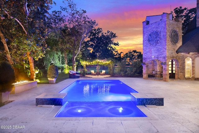 pool at dusk with a patio area and an in ground hot tub