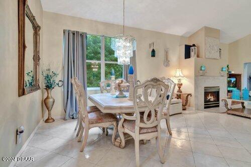 dining area with light tile patterned floors, a lit fireplace, a chandelier, and baseboards