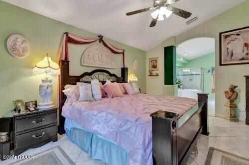 bedroom featuring visible vents, arched walkways, a ceiling fan, ensuite bath, and vaulted ceiling