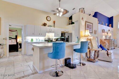 kitchen featuring high vaulted ceiling, stainless steel appliances, a breakfast bar, a peninsula, and light countertops